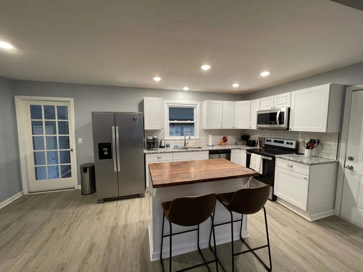 The image features another perspective of the kitchen, focusing on the kitchen island, stainless steel refrigerator, white cabinetry, and a suite of modern appliances. The mood is welcoming and functional, ideal for family gatherings and meal preparation.