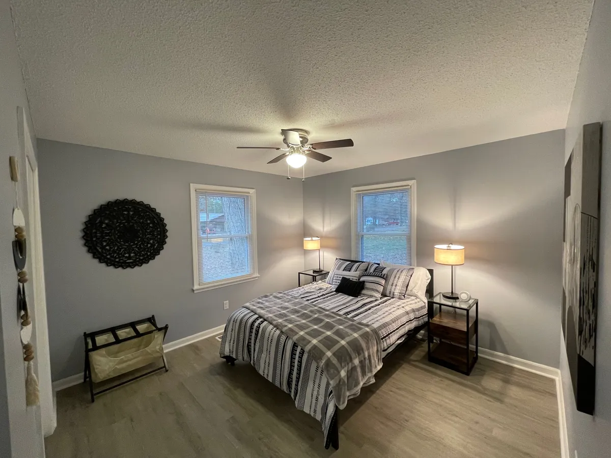 An inviting bedroom with a plush bed, nightstands with lamps, and thoughtful wall decor. Warm lighting and gentle, early morning sunlight create a welcoming, restful mood—ideal for reading, relaxing, or drifting off to sleep.