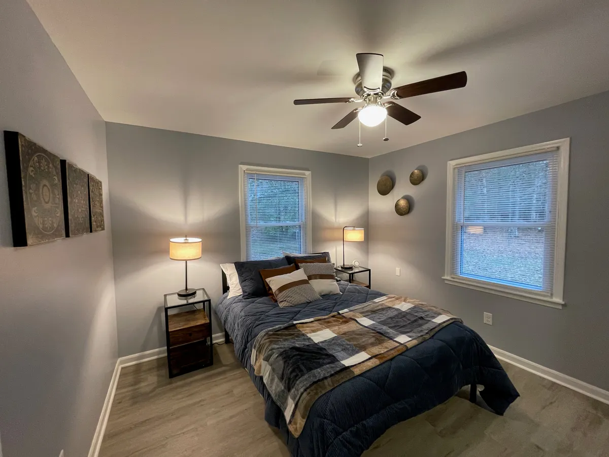 A cozy bedroom featuring a neatly made bed with a patterned throw, flanked by nightstands with softly glowing lamps and decorative wall art above. Natural light filters softly into the room, creating a serene and restful atmosphere perfect for unwinding or getting a peaceful night's sleep.