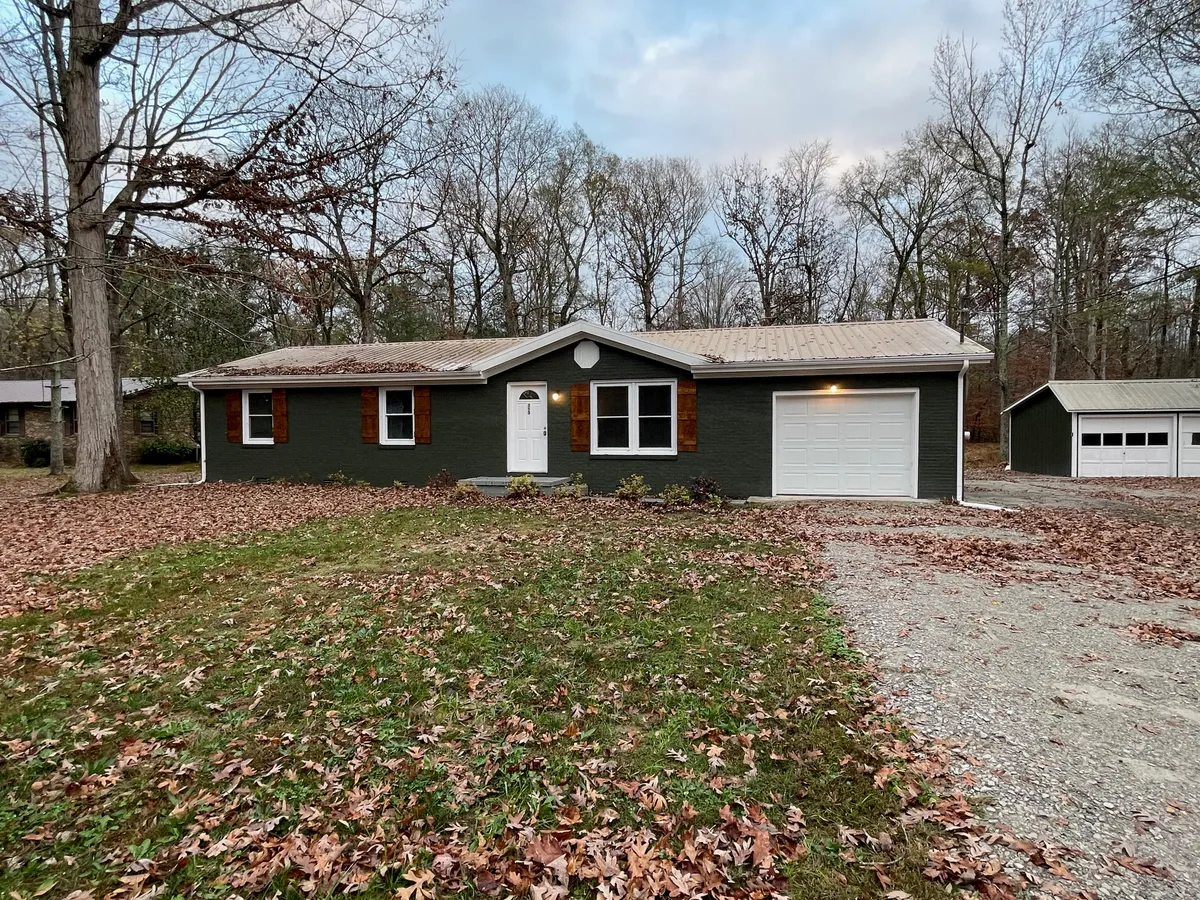 The image captures the charming exterior of a beautifully remodeled single-family cottage in Manchester, Tennessee, featuring a welcoming main entrance, classic shuttered windows, a spacious garage door, and lush surrounding trees. The peaceful yard hints at opportunities for relaxing, enjoying nature walks, or gathering with loved ones outdoors.